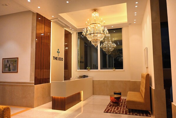 A hotel reception area with a modern design, featuring a reception desk, a chandelier, and a seating area.