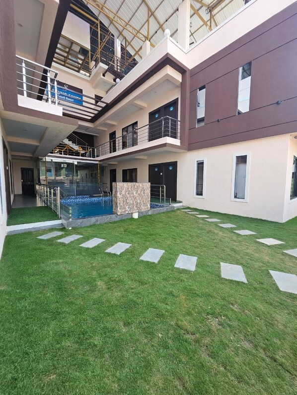 A modern building with a rooftop pool, multiple balconies, and a well-maintained lawn.