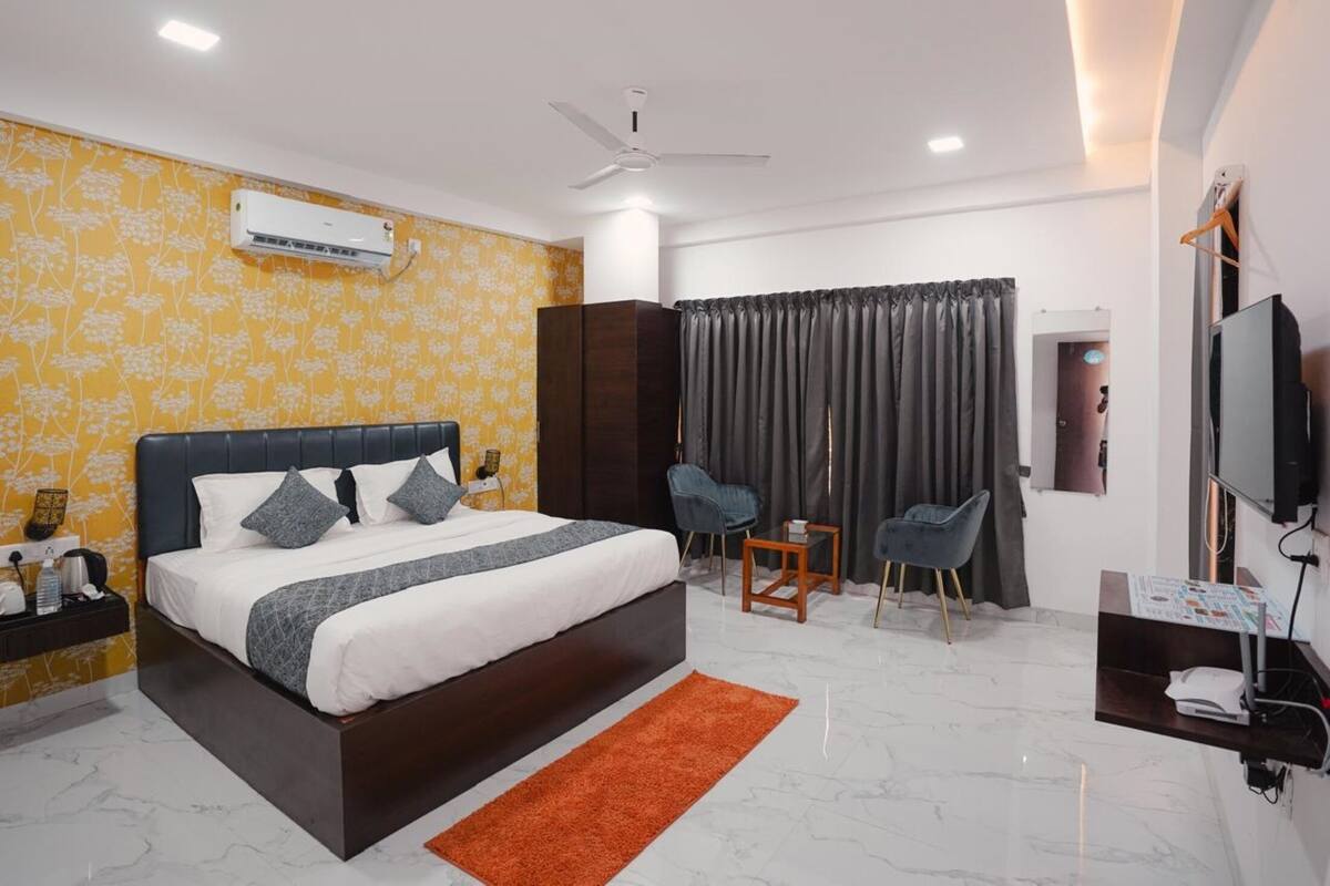 A modern hotel room with a large bed, a ceiling fan, an air conditioning unit, a TV, and a small seating area with chairs.