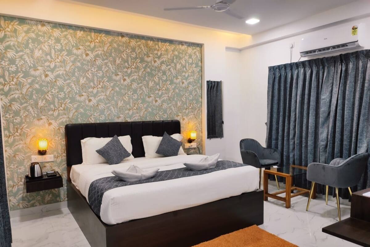 A modern hotel room with a large bed, two bedside lamps, a desk with a chair, and a window with curtains.