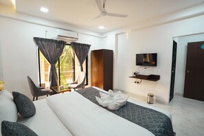 A modern hotel room with a large bed, a desk, a chair, a TV, and a wardrobe. - Singing Sands Beach Resort (Alibag)