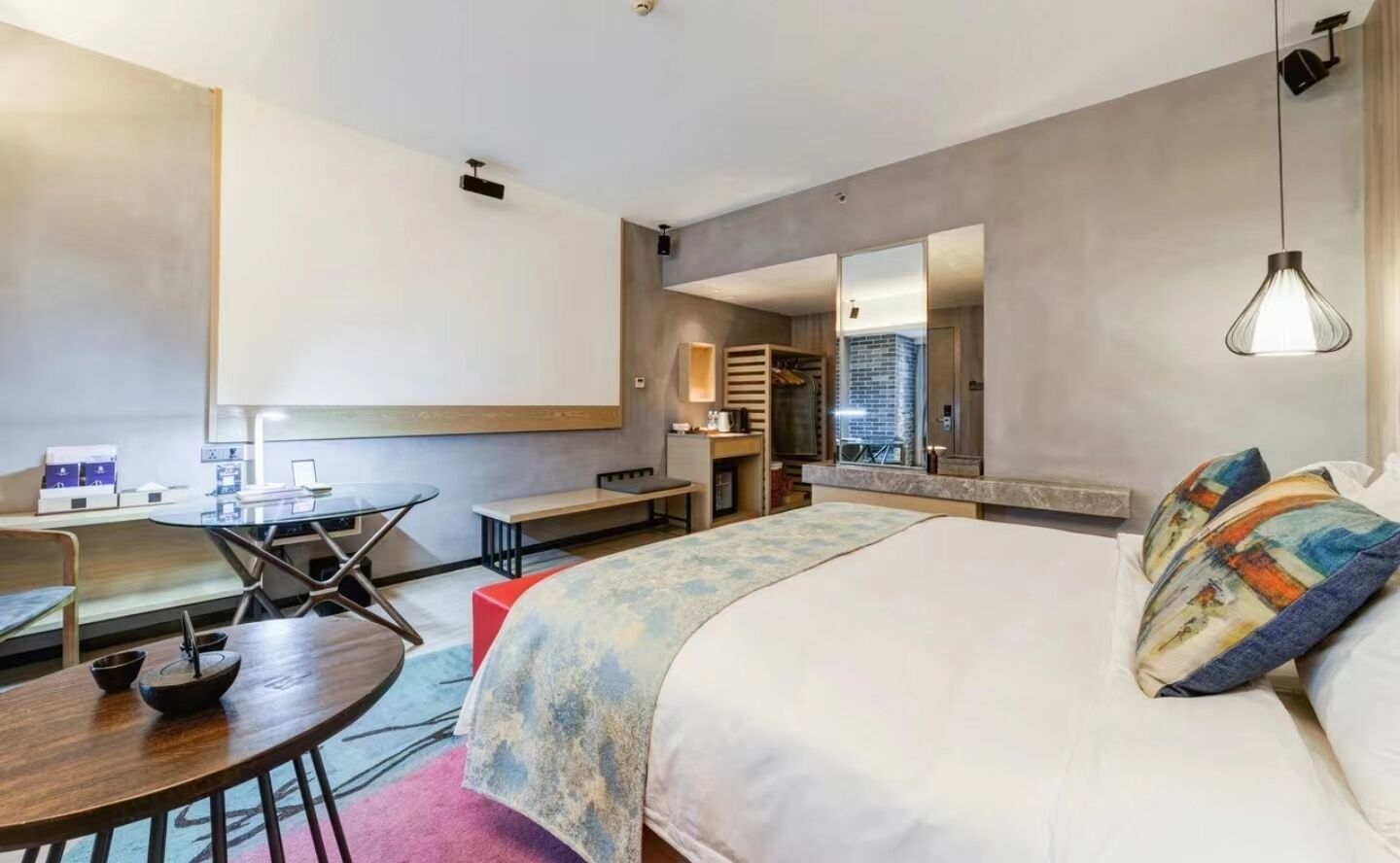 Una habitación de hotel con cama, escritorio, silla, una mesita y un espejo.