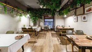 Una sala de reuniones moderna con mesas y sillas de madera, un ventanal grande y plantas de interior.