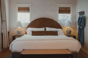 A bedroom with a large bed, two bedside tables with lamps, a bench, and a window with a view. - Swank Suites | Step Free King - Pet Friendly (Ashland)