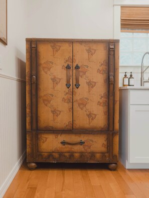 A large wooden cabinet with a world map design, featuring two doors and a drawer, situated in a room with a wooden floor and a window with blinds. - Swank Suites | Step Free King - Pet Friendly (Ashland)