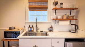 Una cocina con un fregadero, microondas y estantes con utensilios de cocina.