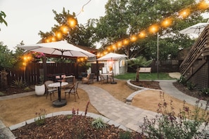 Un patio al aire libre con luces colgantes, una zona de estar cubierta y un sendero.