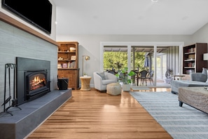 Una sala de estar moderna con chimenea, suelo de madera y un ventanal con vistas a un jardín.