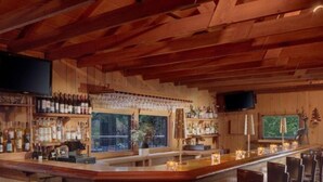 A wooden bar area with shelves of bottles and glasses, a TV mounted on the wall, and a view of the outdoors.