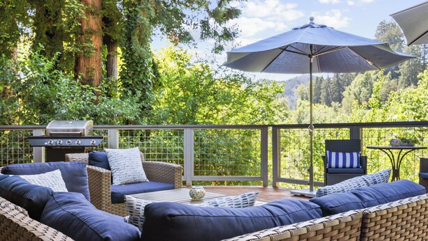 A deck with wicker furniture, a grill, and a large umbrella.