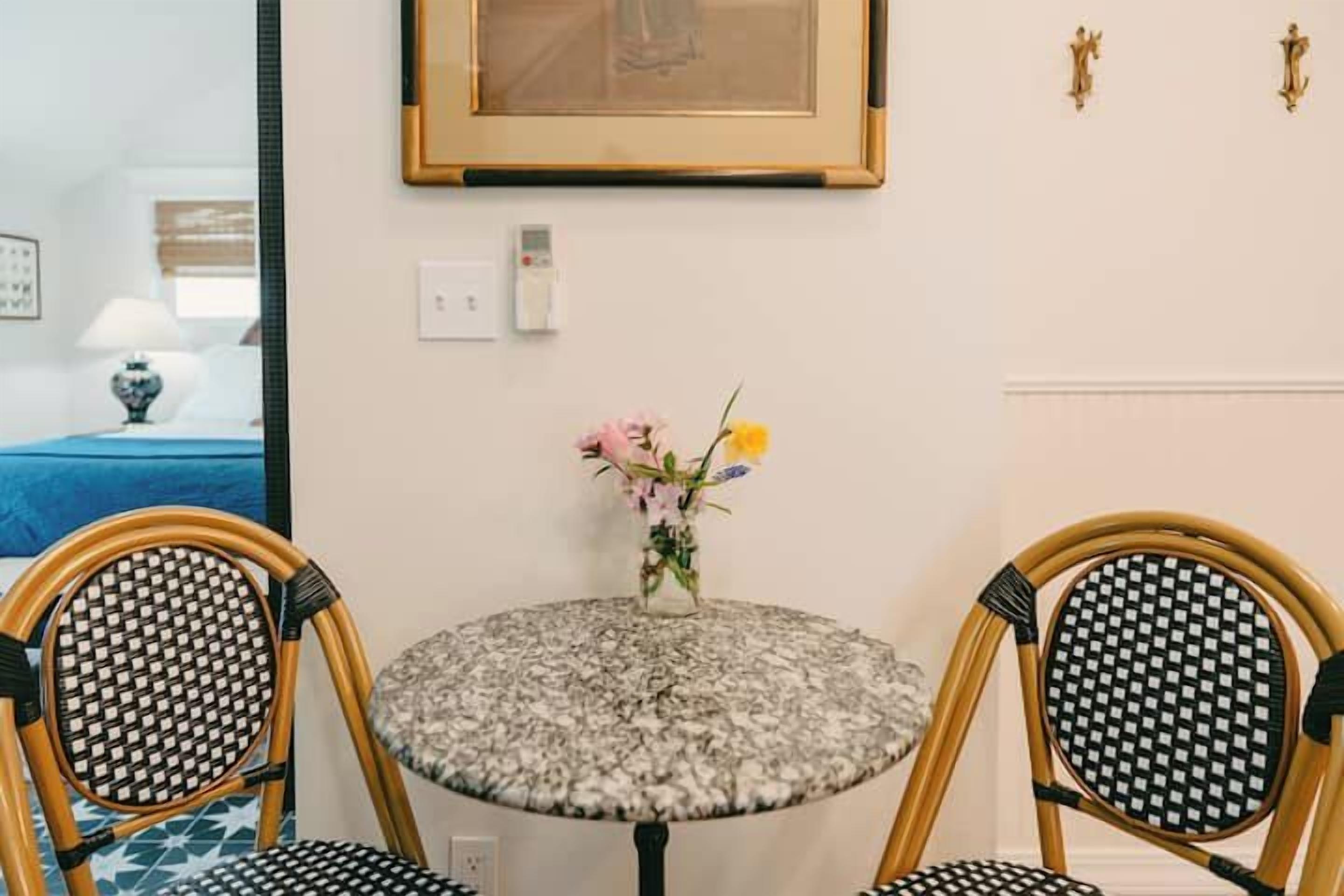 A round table with a floral-patterned tablecloth, two wicker chairs, and a vase with flowers.