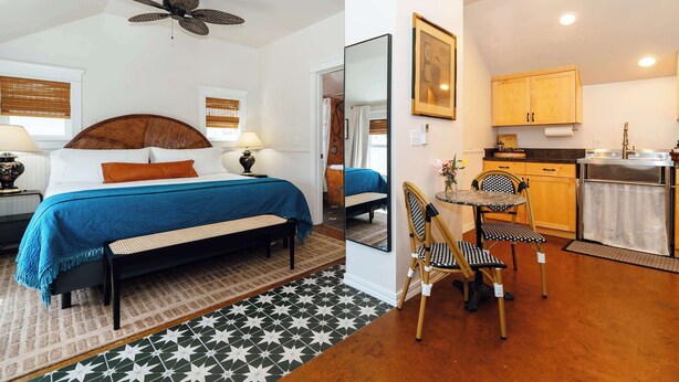 Une chambre d’hôtel équipée d’un lit, d’une table de chevet, d’une lampe, d’un ventilateur de plafond et offrant une vue sur la cuisine.