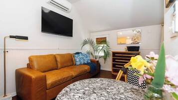 A living room with a sofa, a round table, a TV mounted on the wall, and a potted plant.