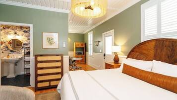 A bedroom with a large bed, a wooden headboard, a bedside table with a lamp, a dresser, and a bathroom with a sink and mirror.