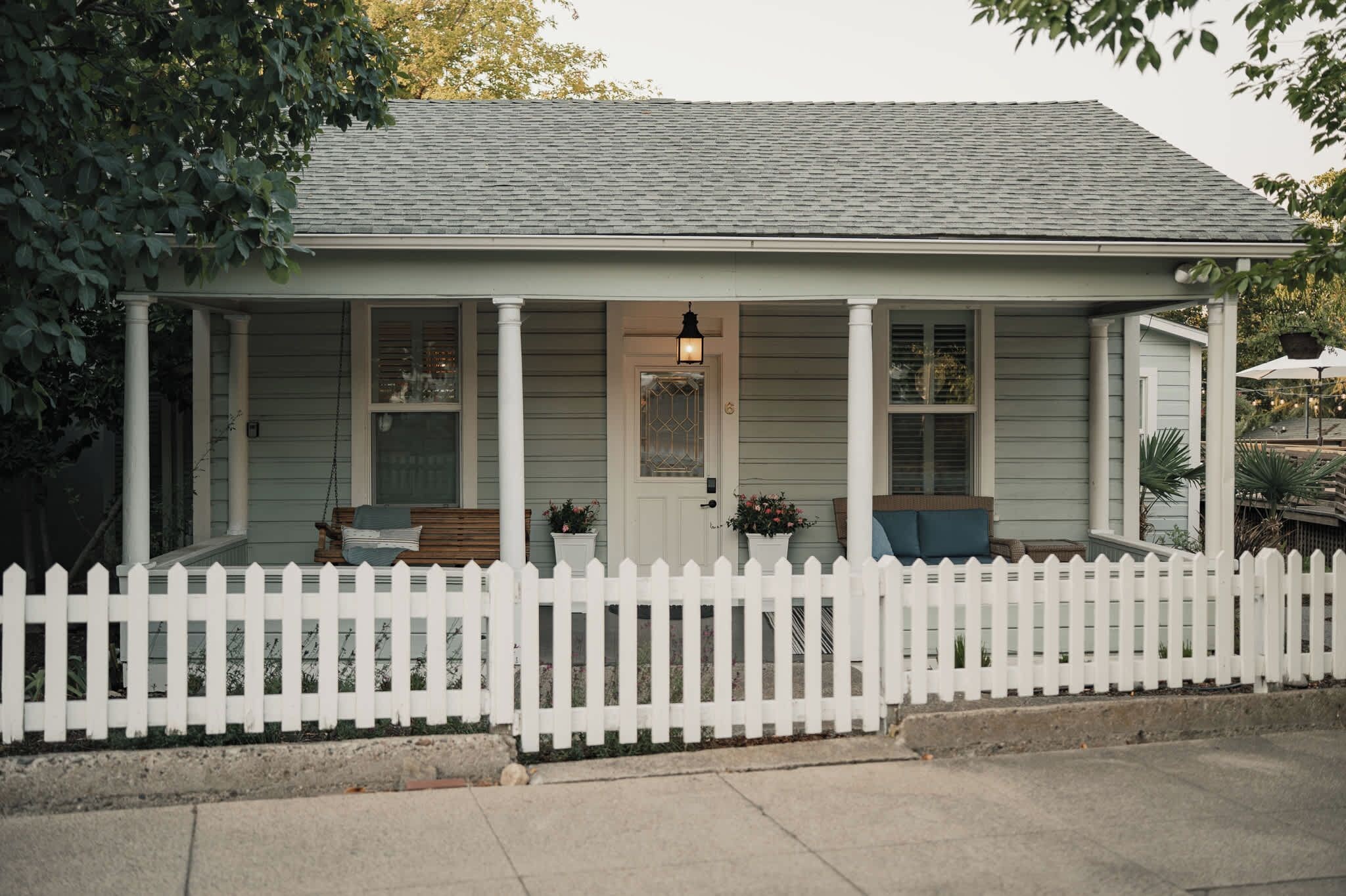 Ein einstöckiges Haus mit Veranda, weißem Zaun und kleinem Garten.