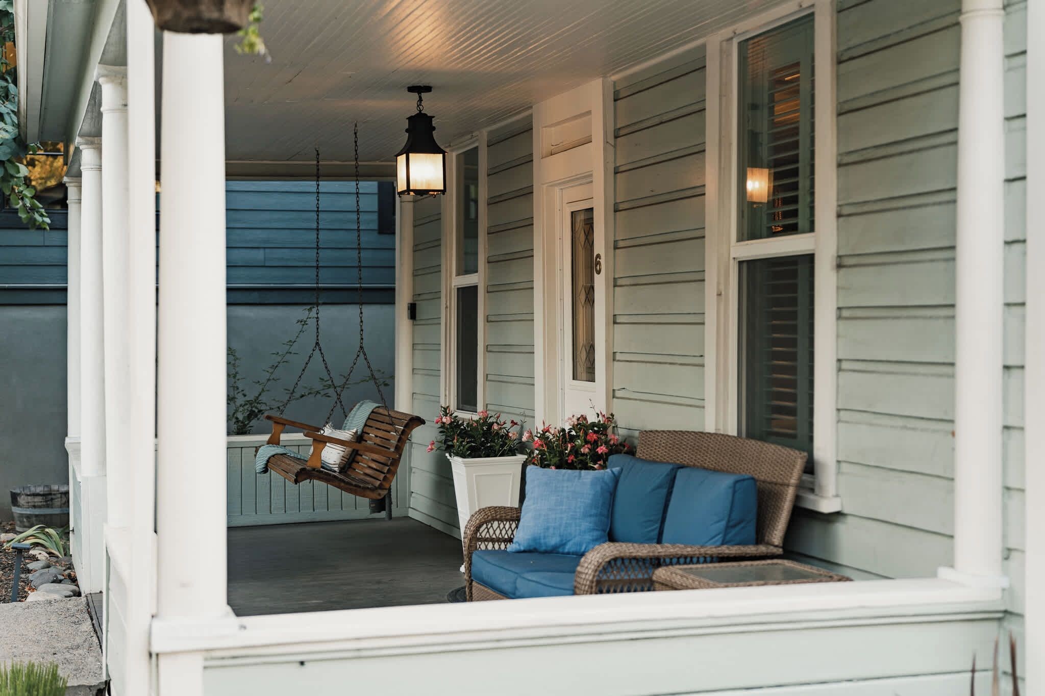 A porch with a swing chair, a wicker sofa, and a potted plant.