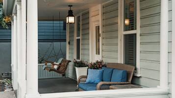 A porch with a swing chair, a wicker sofa, and a potted plant.