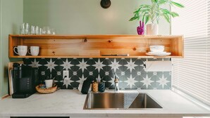 A kitchen with a wooden shelf, a coffee maker, a sink, and a patterned backsplash. - Swank Suites + Private Porch Patio (Ashland)