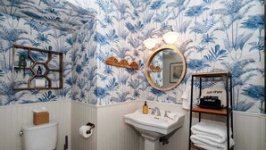 A bathroom with a toilet, sink, and mirror. There is a shelf with towels and a hair dryer. - Swank Suites + Private Porch Patio (Ashland)