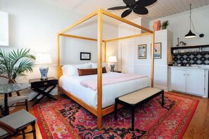 A four-poster bed with a bench, a small table, and a chair in a bedroom with a patterned rug.