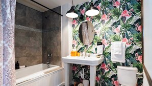 A bathroom with a bathtub, a sink, and a toilet. There is a shower curtain, a mirror, and a towel hanging on the wall. - Swank Suites | King with Lux Tub (Ashland)