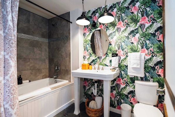 A bathroom with a bathtub, a sink, and a toilet. There is a shower curtain, a mirror, and a towel hanging on the wall. - Swank Suites | King with Lux Tub (Ashland)