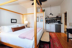 Een kamer met een hemelbed, een kleine kitchenette en een rood tapijt met een patroon.