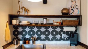 A kitchen with a marble countertop, a stainless steel sink, a coffee maker, and a decorative shelf with a giraffe figurine and a basket. - Swank Suites | King with Lux Tub (Ashland)