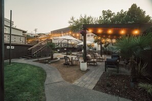 Un espacio de patio al aire libre con una pérgola, mobiliario y una escalera que lleva a un nivel superior.