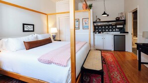 A bedroom with a four-poster bed, a small kitchenette, and a wooden ceiling. - Swank Suites | King with Lux Tub (Ashland)