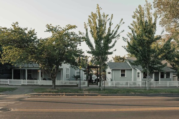 A residential street with houses, a white picket fence, and trees.