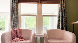 A room with two armchairs facing a large window with a view of trees. - Swank Boutique Suites | King Suite | DT Ashland (Ashland)