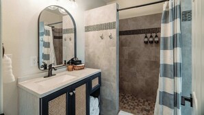 A bathroom with a sink, mirror, and shower area. - Swank Boutique Suites | King Suite | DT Ashland (Ashland)