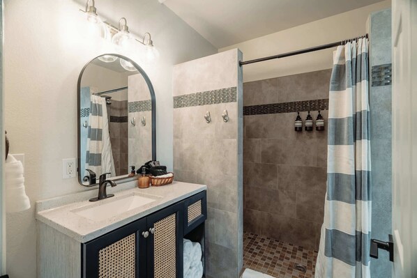 A bathroom with a sink, mirror, and shower area. - Swank Boutique Suites | King Suite | DT Ashland (Ashland)