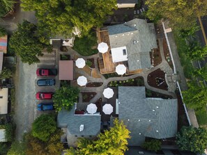 An aerial view of a residential area with multiple houses, a parking lot with several cars, and a central open space with umbrellas.