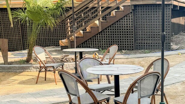 An outdoor patio area with a round table and four wicker chairs, surrounded by striped umbrellas. - Swank Suites | King with Lux Tub (Ashland)