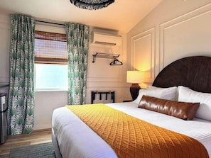 Una habitación de hotel con una cama grande, una mesita de noche, una lámpara y una ventana con cortinas.