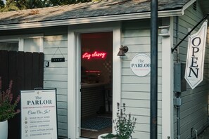 En byggnad med en skylt som visar texten ”The Parlor” och ordet ”ÖPPET” på dörren, vilket tyder på att det är en affärslokal.