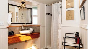 Un baño con un lavamanos blanco, estantes de madera, un espejo, una lámpara con forma de estrella, una cortina de ducha y cuadros en la pared.