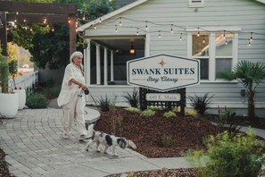 Señal de Swank Suites con el lema 'Stay Classy', un camino pavimentado y un perro paseando.