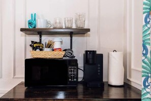 En køkkenbordplade med mikrobølgeovn, kaffemaskine og en kurv med snacks.