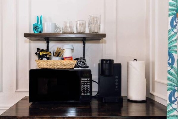 A kitchen counter with a microwave, coffee maker, and a basket of snacks.