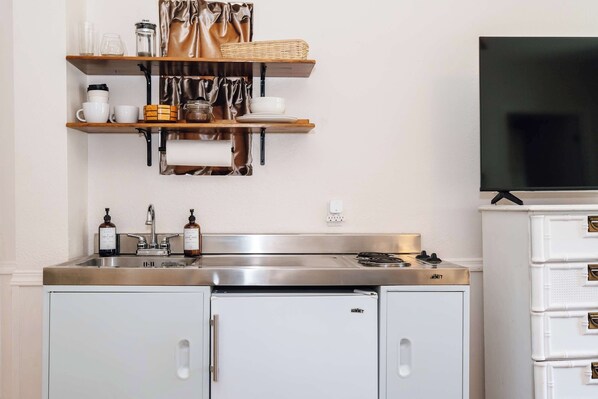 A kitchen with a stainless steel sink, white cabinets, a built-in stove, and a flat-screen TV above the cabinets.