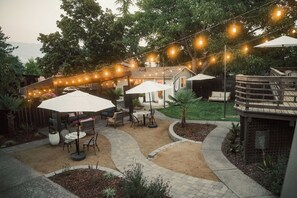Un espace extérieur aménagé en terrasse, avec des guirlandes lumineuses, des parasols et des meubles de jardin.