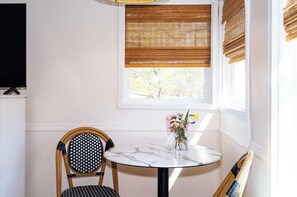 Habitación de esquina con una mesa redonda, dos sillas, un televisor y una ventana con persianas.