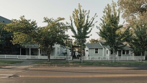 Une rangée de maisons de plain-pied, avec une clôture en bois peinte en blanc, un ciel dégagé et une rue au premier plan.