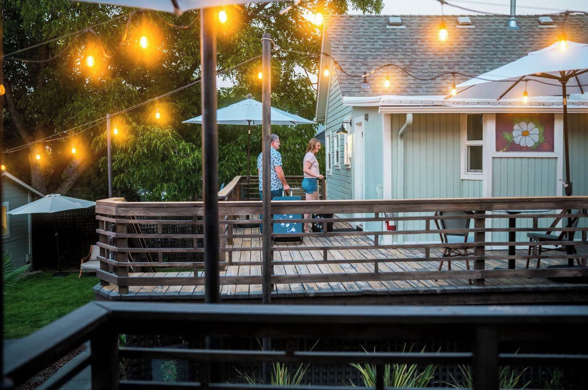 A wooden deck with a railing, string lights, and a building with a window and a flower mural.