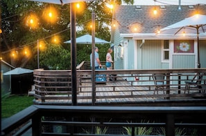 Een houten terras met een balustrade, lichtjes en een gebouw met een raam en een bloemenmuur.