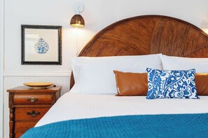 Un lit bien fait, avec une couverture bleue, une tête de lit en bois et un tableau encadré accroché au mur.