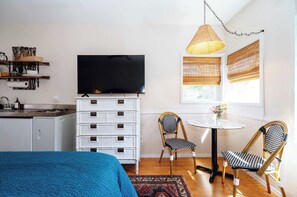 Een compacte hotelkamer met een bed, een televisie, een klein eettafeltje, twee stoelen, een dressoir en een raam met zonwering.